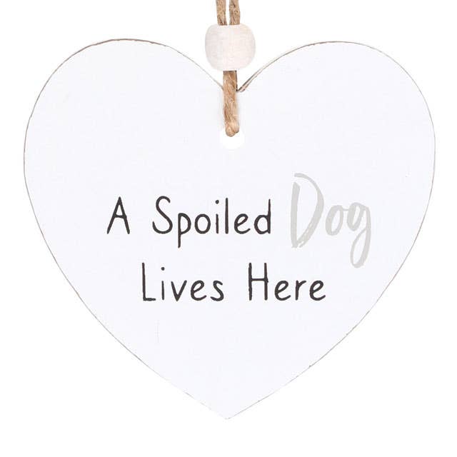 close up of a heart shaped sign which reads a spoilt dog lives here, suspended by a piece of twine and finished with a wooden bead