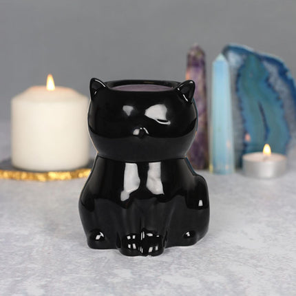 the front view of a shiny black cat fragrance wax warmer in front of some burning candles