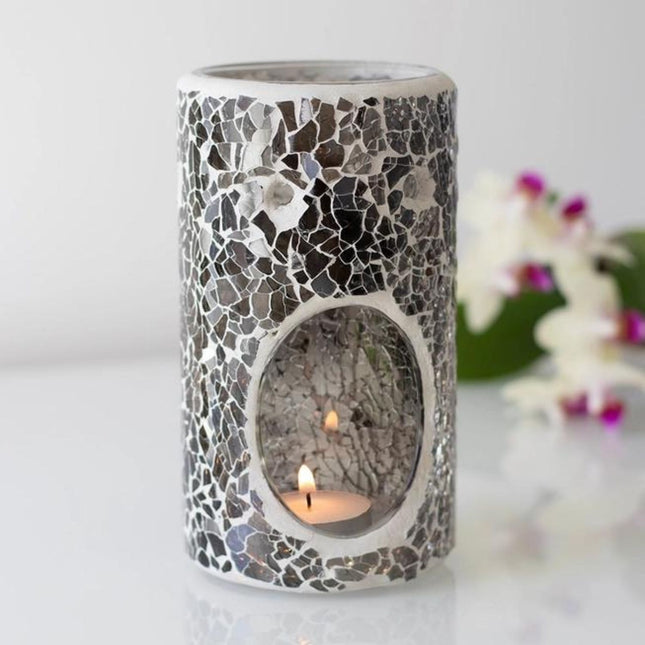 The Scented Wax Melter Oil Burner Pillar by Something Different Wholesale features a grey crackle design and comes with a free melt bar. It resembles a modern holder with a lit tea light, set against softly blurred white and purple flowers.