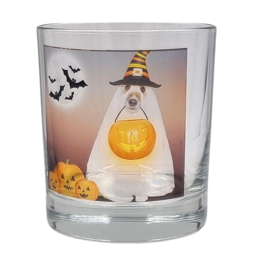 A scented Halloween candle glass featuring a spooky dog in a sheet dressed as a ghost with a trick or treat pumpkin bowl