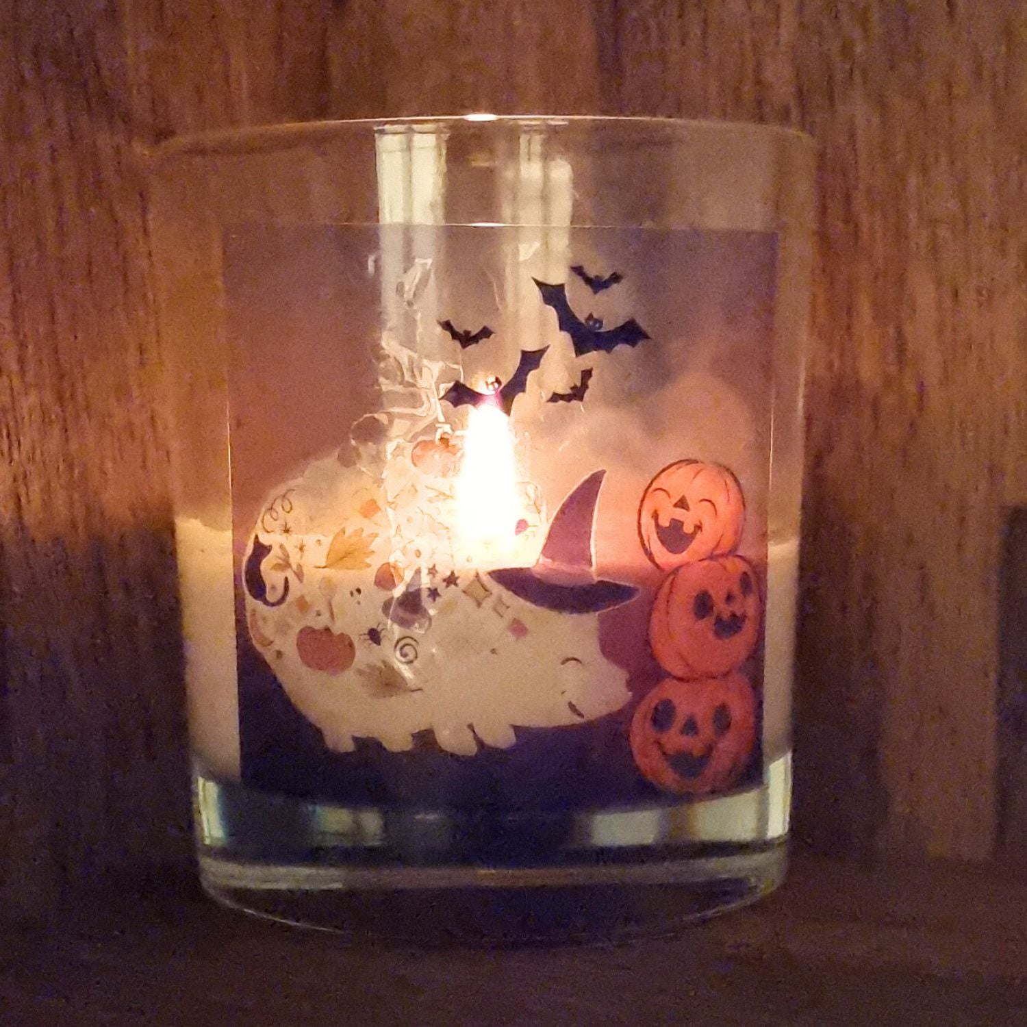 a lit scented halloween candle in glass with a cute hedgehog in a witches hat with pumkins and bats