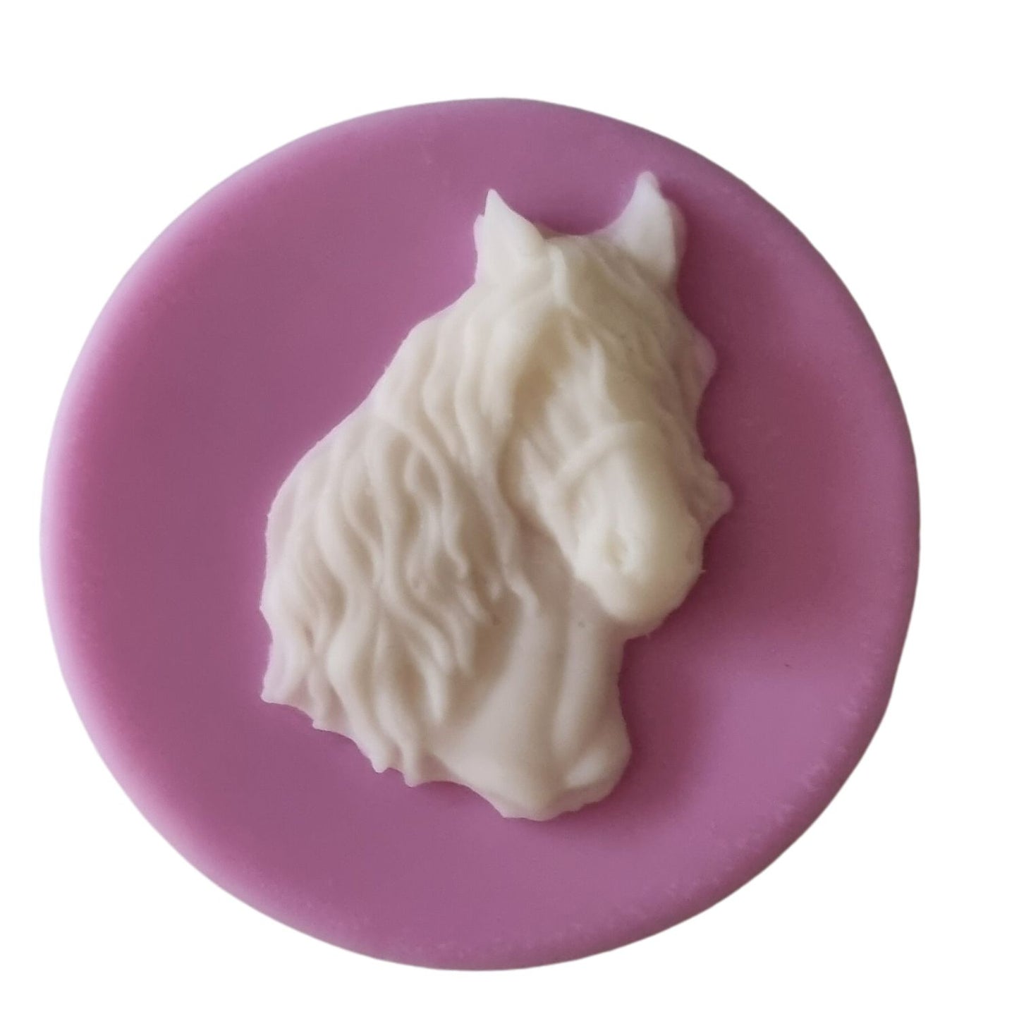 A pink coloured disc shaped wax melt with a white wax horses head with a flowing mane and forelock.