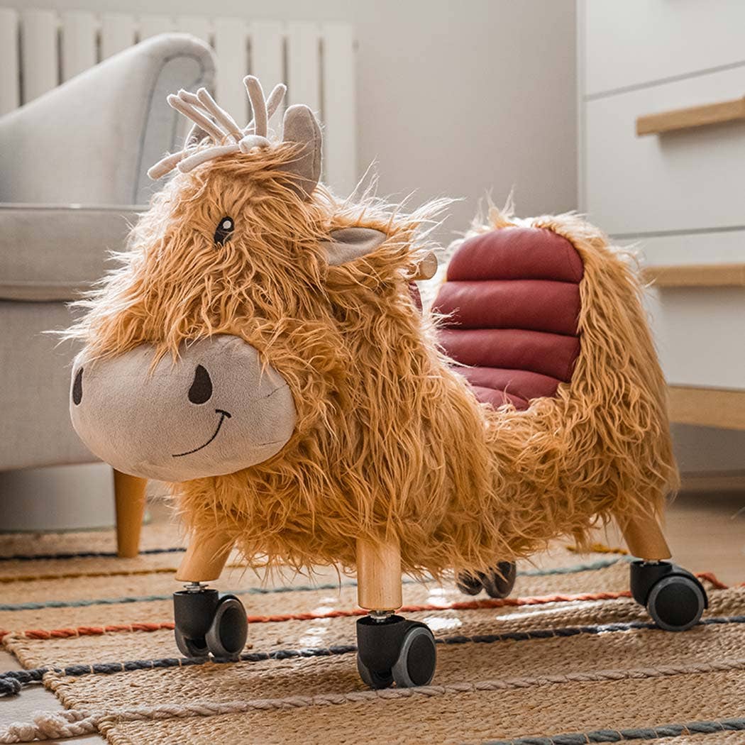 a gorgeous highland cow ride on toy with golden fur, a loveable smiley face, leatherette seat and multi directional castors in a living room setting