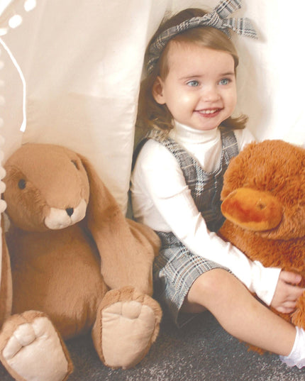 A smiling child in a plaid dress hugs the Jomanda Soft Toys Large Highland Cow Teddy Plush Baby Soft Toy beside a plush bunny inside a play tent; both toys are machine washable for easy care.