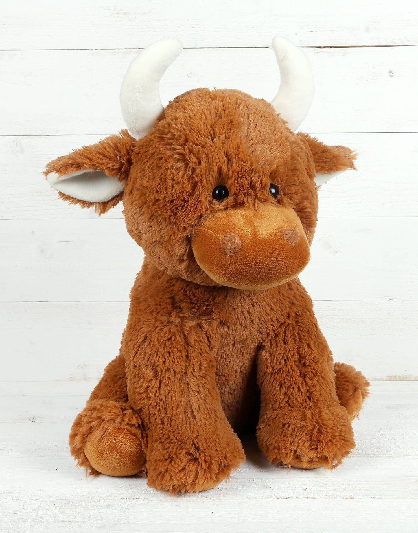 The Large Highland Cow Teddy Jomanda Plush Baby Soft Toy by Jomanda Soft Toys & Accessories sits upright with white horns against a white wooden background. This adorable plush is machine washable for easy care.