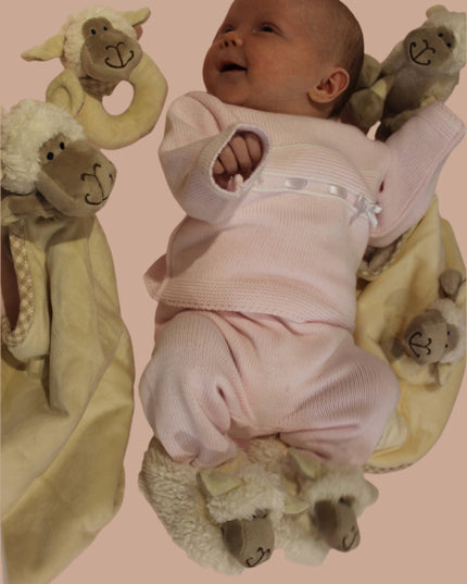 a smiling baby surrounded by the jomanda sheep baby range including toys, soother, baby boots and rattle