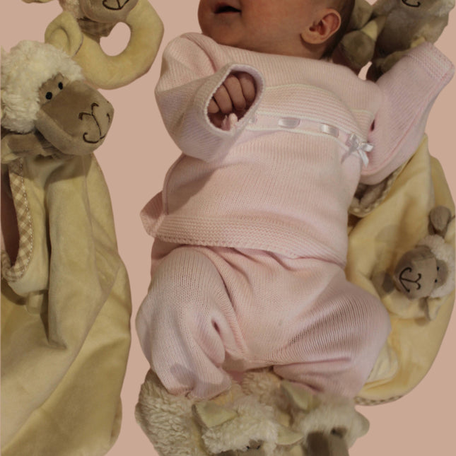 a smiling baby surrounded by the jomanda sheep baby range including toys, soother, baby boots and rattle