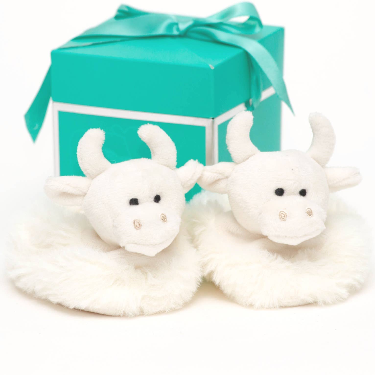  a pair of fluffy cream highland cow baby boots from Jomanda toys in front of a turquoise gift box