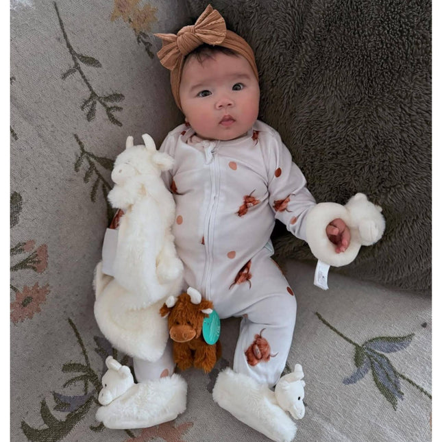 a baby snuggling up to the cream highland cow soother,  rattle and wearing the cream highland cow baby boots