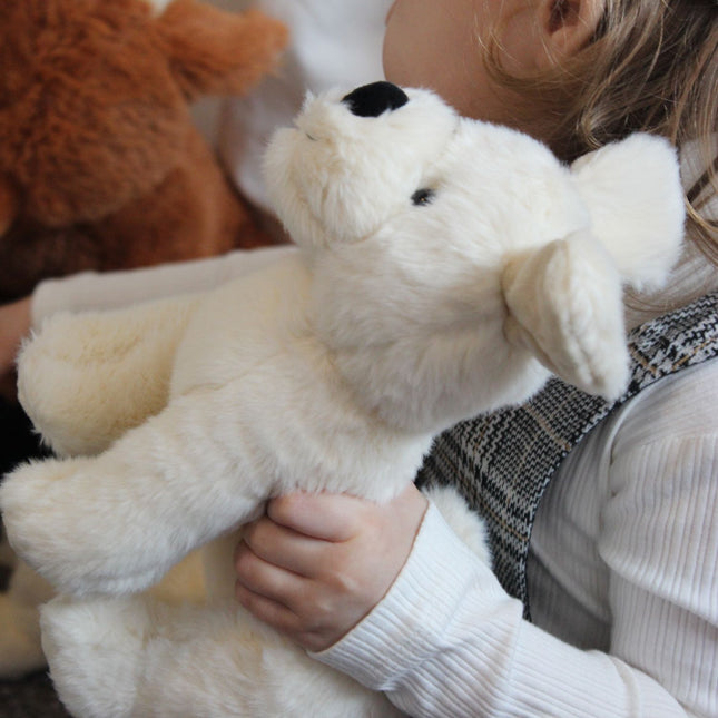 An adorably cute fluffy cream coloured puppy dog from Jomanda toys with black nose and eyes being held by a baby