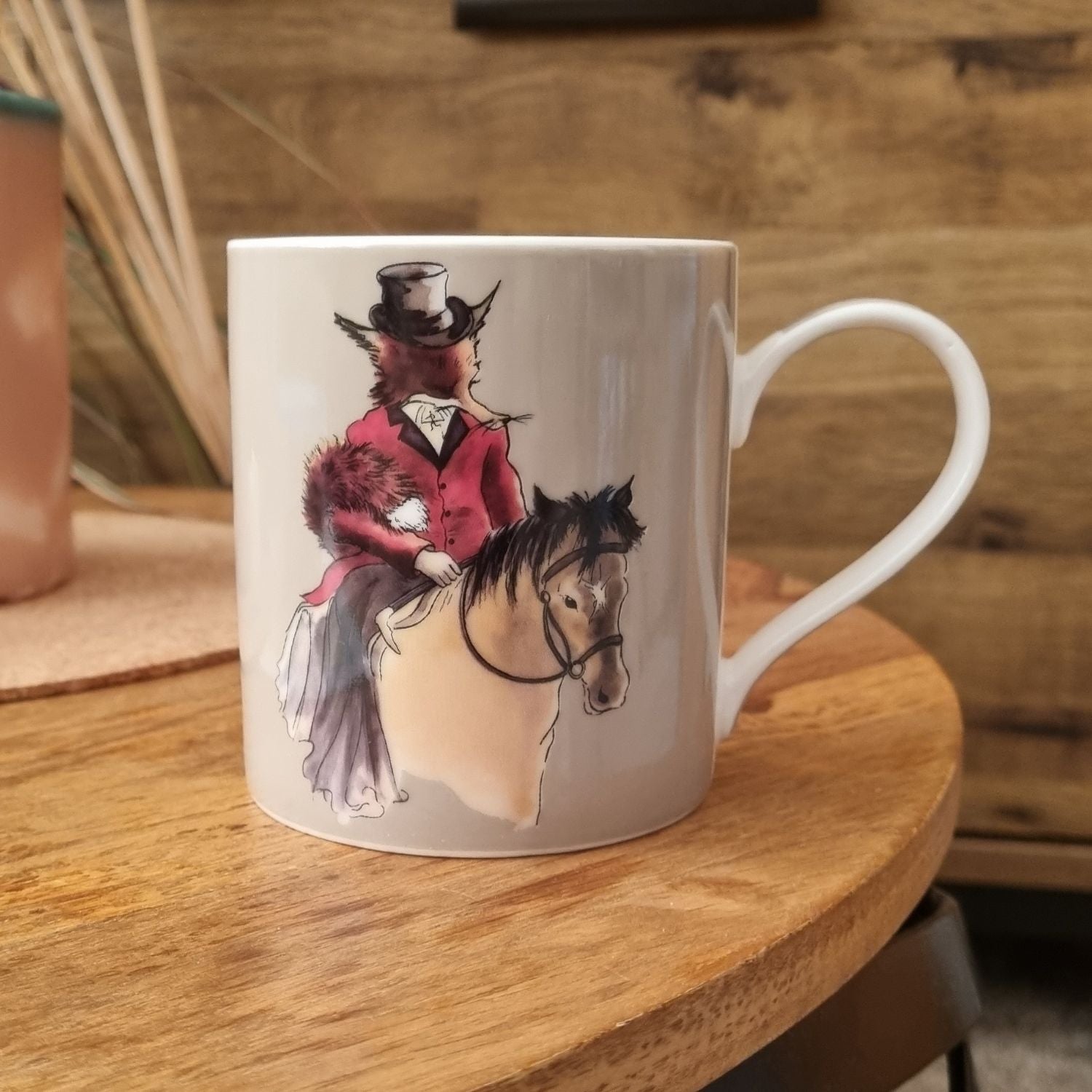 a mug with lady fox design in traditional hunting dress riding a pony the mug is resting on a coffee table