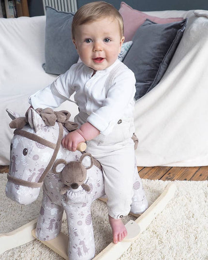 a happy baby riding a cute fabric rocking horse with brown bridle and mane on wooden rockers with a soft toy mouse in a pocket on the horses shoulder