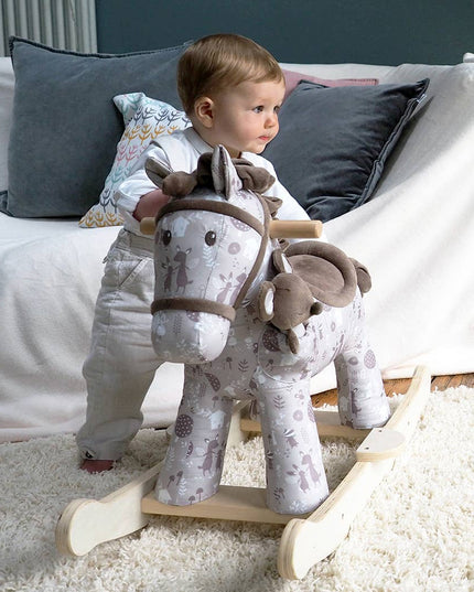 a baby standing next to a cute fabric horse with brown bridle, saddle, mane and tail on wooden rockers with a soft toy mouse in a pocket on its shoulder