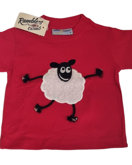 The Ramblers Sheep Embroidered T Shirt Red With Applique Dangly Leg Lamb features a smiling cartoon sheep with black limbs and a fluffy white body. Made from 100% cotton, this toddler tee is machine washable and has a Ramblers tag on the collar.