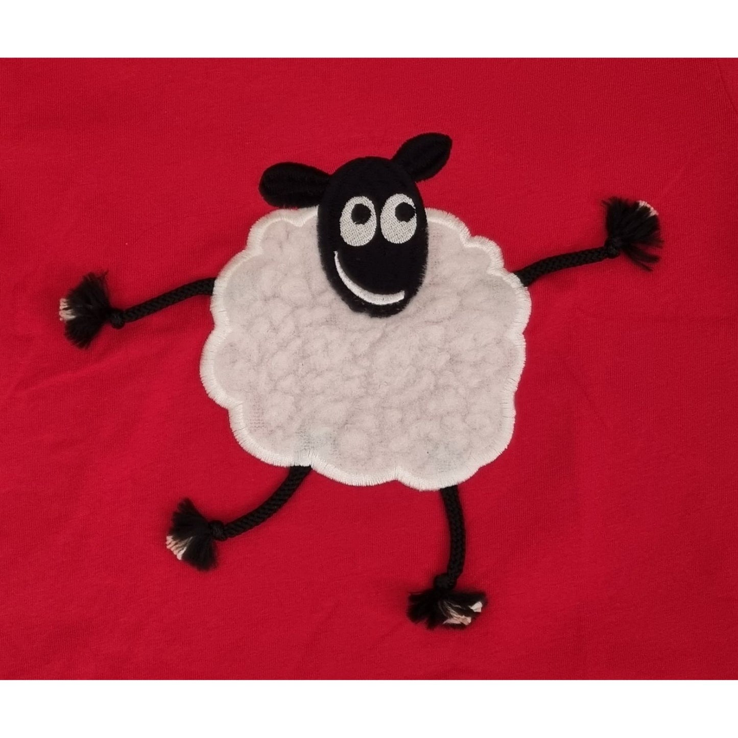 A playful Sheep Embroidered T Shirt Red With Applique Dangly Leg Lamb by Ramblers features a smiling cartoon lamb with rope limbs on a bright red, 100% cotton, machine washable teeâ€”perfect for animal lovers.