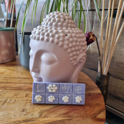 A lilac Scented Wax Melt bar with love and white paw prints resting against a buddha head wax warmer