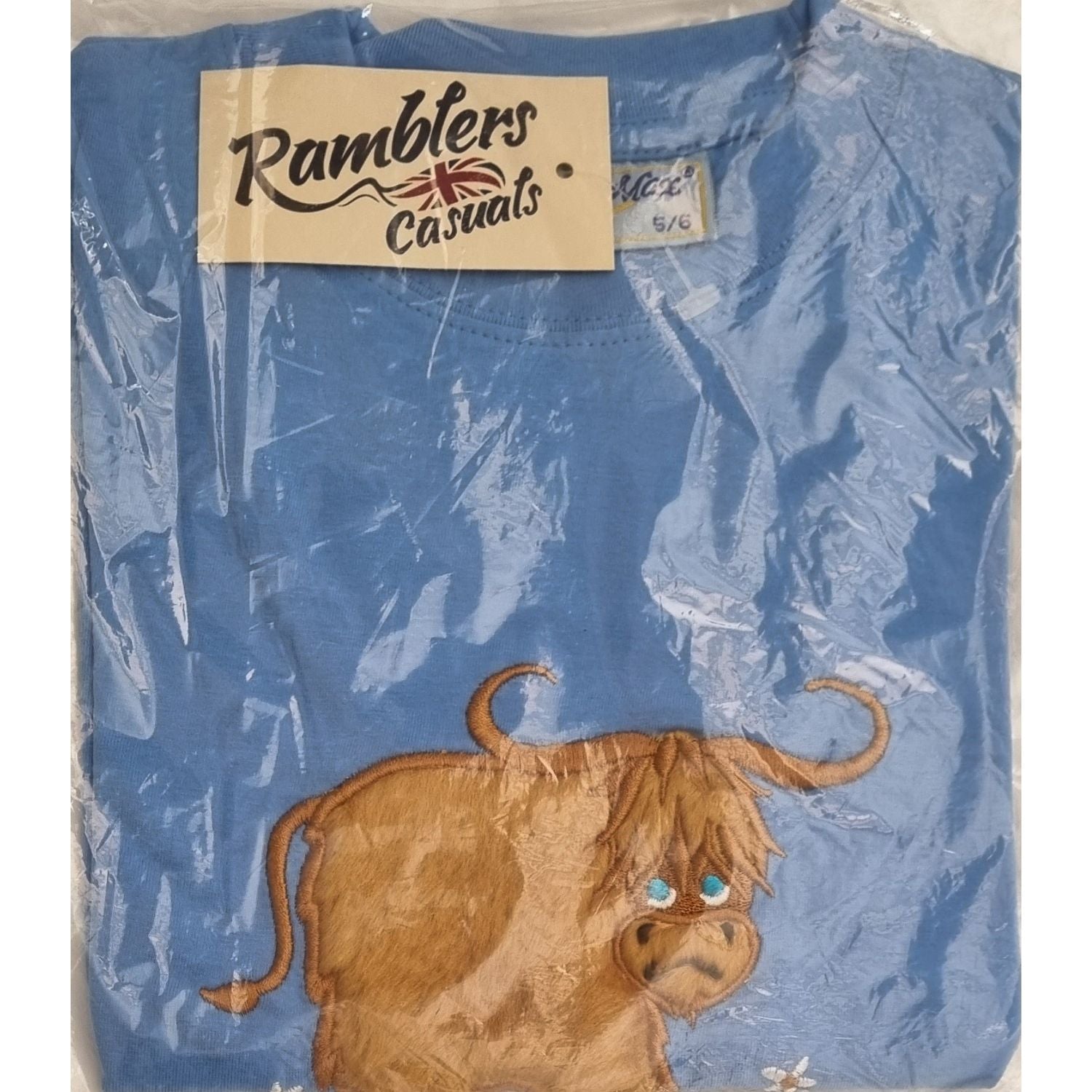 A folded blue 100% cotton Ramblers Highland Cow Embroidered T Shirt MacMoo Design for children, packaged in clear plastic. Features an embroidered cartoon highland cow with shaggy brown fur and blue eyes.