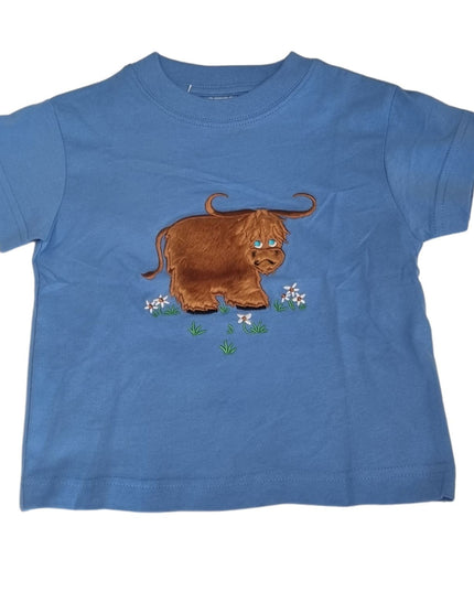 The Ramblers Highland Cow Embroidered T Shirt MacMoo Design for children is a blue, short-sleeved 100% cotton tee featuring a fuzzy brown highland cow on grass with white flowers, offering all-day comfort.