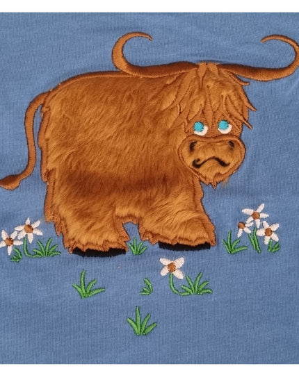 The Ramblers Highland Cow Embroidered T Shirt MacMoo Design for children features a cartoon-style highland cow with long brown fur and blue eyes on grass with white flowers, all on soft 100% cotton.