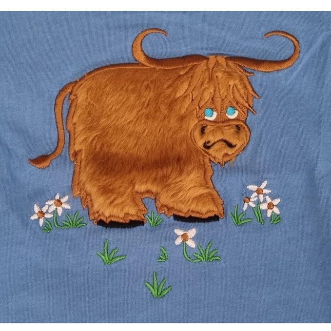The Ramblers Highland Cow Embroidered T Shirt MacMoo Design for children features a cartoon-style highland cow with long brown fur and blue eyes on grass with white flowers, all on soft 100% cotton.