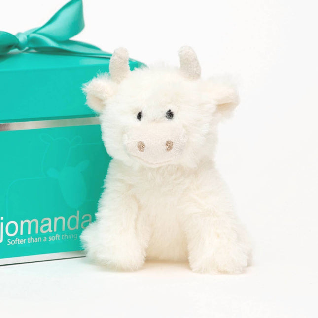 a cute cream highland cow with horns made of soft plush fur next to a jomanda branded gift box
