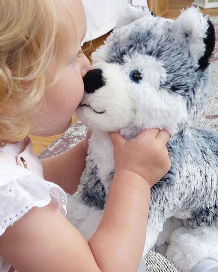 a baby girl kissing a silver and white soft toy husky dog on the nose