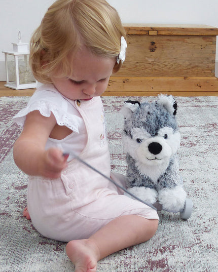 a baby girl playing with a pull along soft toy husky dog on wheels.