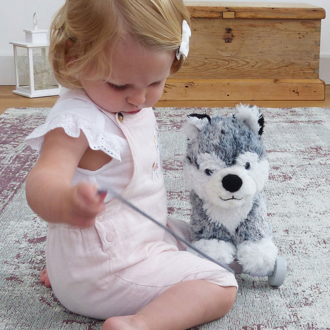 a baby girl playing with a pull along soft toy husky dog on wheels.
