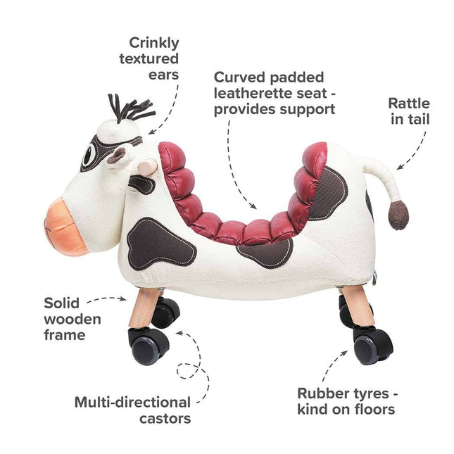 The Moobert Cow Ride On Toy by Little Bird Told Me UK is a wooden ride-on for toddlers with a curved padded seat, crinkly ears, tail rattle, solid wood frame, rubber tyres, and multi-directional castors. Labels highlight each fun feature.