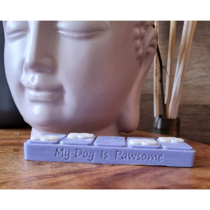 the side view which reads my dog is pawsome of a blue wax melt bar with white paw prints on a wooden table next to a buddha head wax warmer
