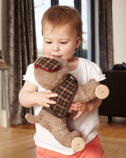 a baby cuddling a cute  beige coloured soft toy puppy dog with a checked jacket and ears