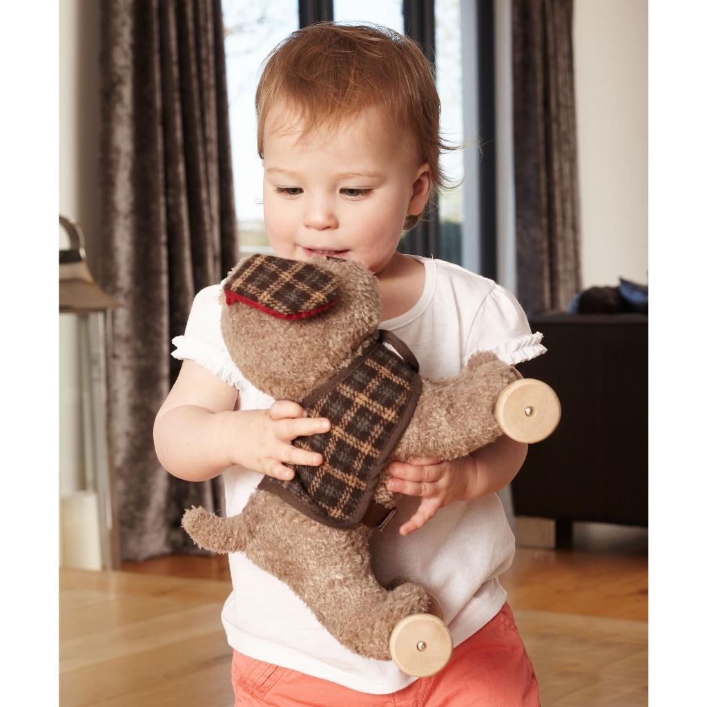 a baby cuddling a cute  beige coloured soft toy puppy dog with a checked jacket and ears
