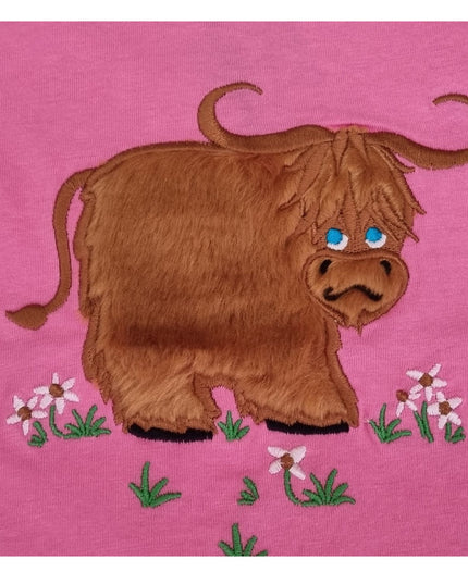 The Ramblers Highland Cow Embroidered T Shirt MacMoo Design features a shaggy brown cow with blue eyes on pink 100% cotton, standing on grass with pink and white flowersâ€”a cute childrens tee.
