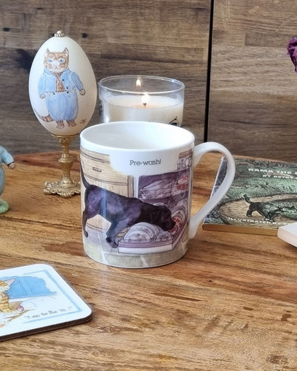 The Dog Mug Alisons Animals Pre-wash Cartoon Gift Boxed by Alisons Animals, featuring a playful dog design and Pre-wash! sits among cat figurines, a candle, coaster, book, and dried rose—perfect as a gift for animal lovers.
