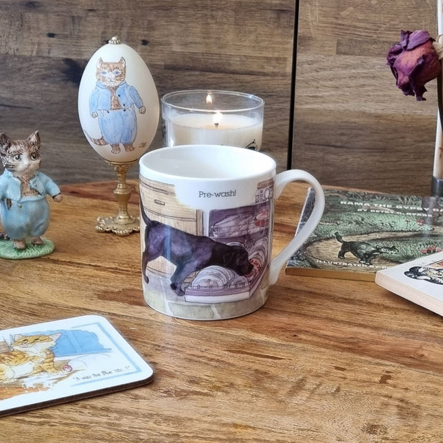 The Dog Mug Alisons Animals Pre-wash Cartoon Gift Boxed by Alisons Animals, featuring a playful dog design and Pre-wash! sits among cat figurines, a candle, coaster, book, and dried rose—perfect as a gift for animal lovers.