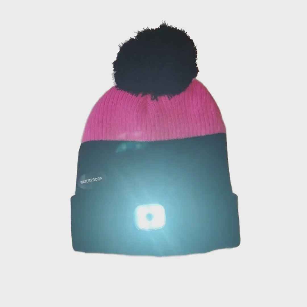 a black and pink bobble hat with a large black bobble and an LED light on the headband switched on to flashing mode