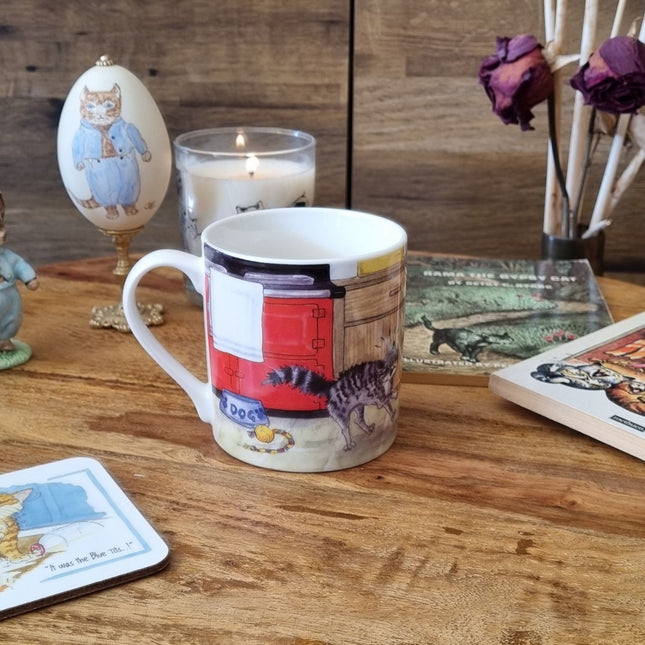 The Dog Mug Alisons Animals Pre-wash Cartoon Gift Boxed by Alisons Animals, with a fun cat and dog illustration, sits among books, dried roses, a candle, an egg, and cat-themed cards—an ideal gift for animal lovers.