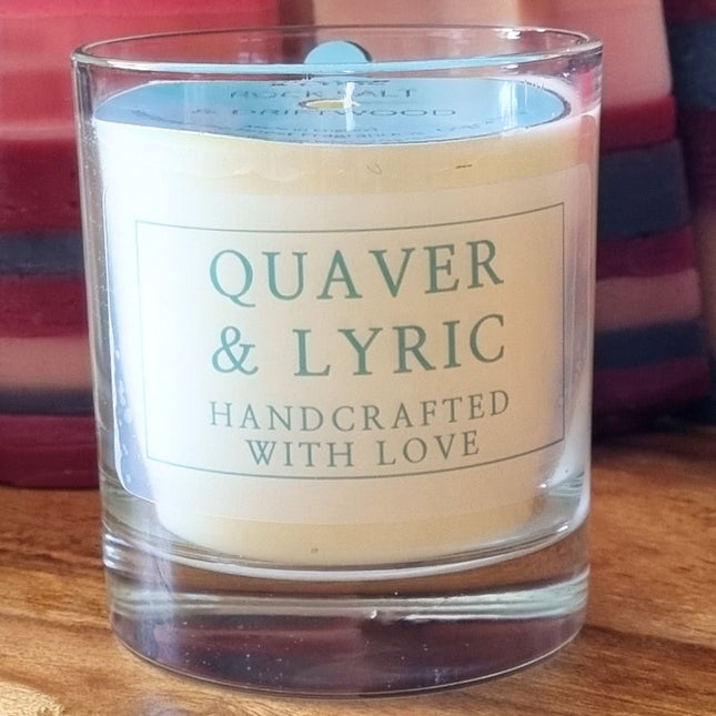 a candle in a glass with quaver & lyric handcrafted with love label and blue dust cover