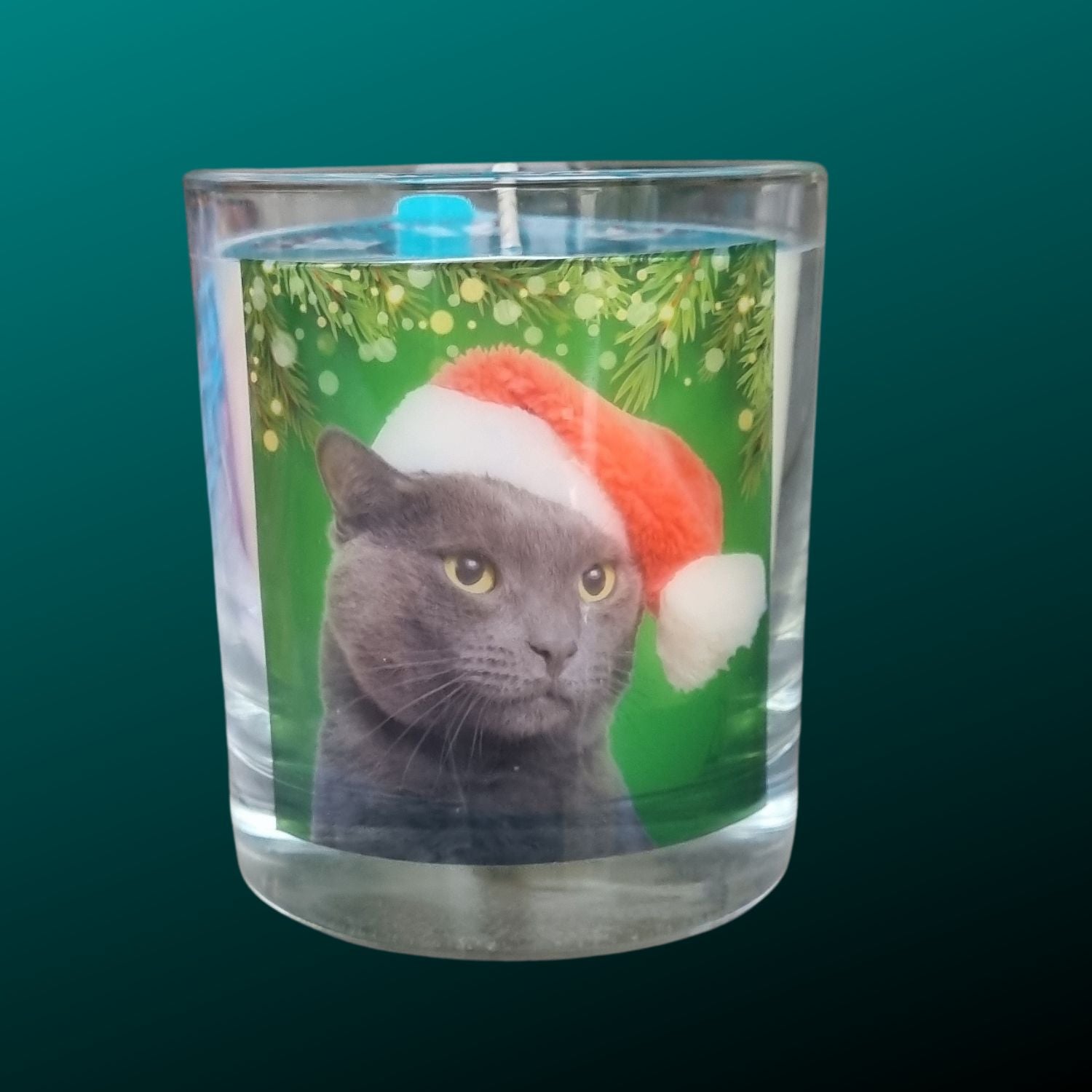 A scented candle in a glass container with a cute grey cat in a Santa hat.