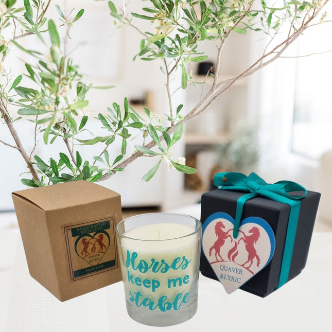 The Quaver&Lyric Scented Candle In Glass Container features a â€œHorses Keep Me Stableâ€ design and premium fragrance, packaged in a brown box and black gift box with teal ribbonâ€”an ideal horse loverâ€™s gift on a bright, leafy table.