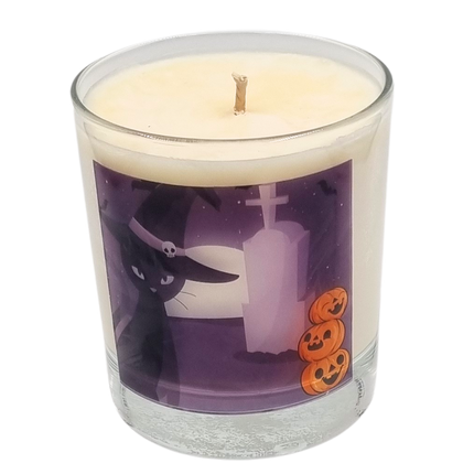 glass container halloween candle with black cat in witches hat in a graveyard with pumpkins