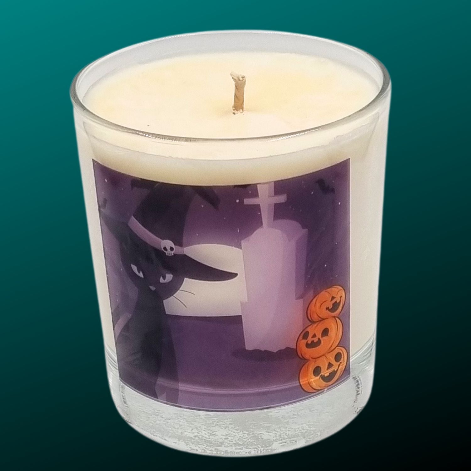 glass container halloween candle with black cat in witches hat in a graveyard with pumpkins