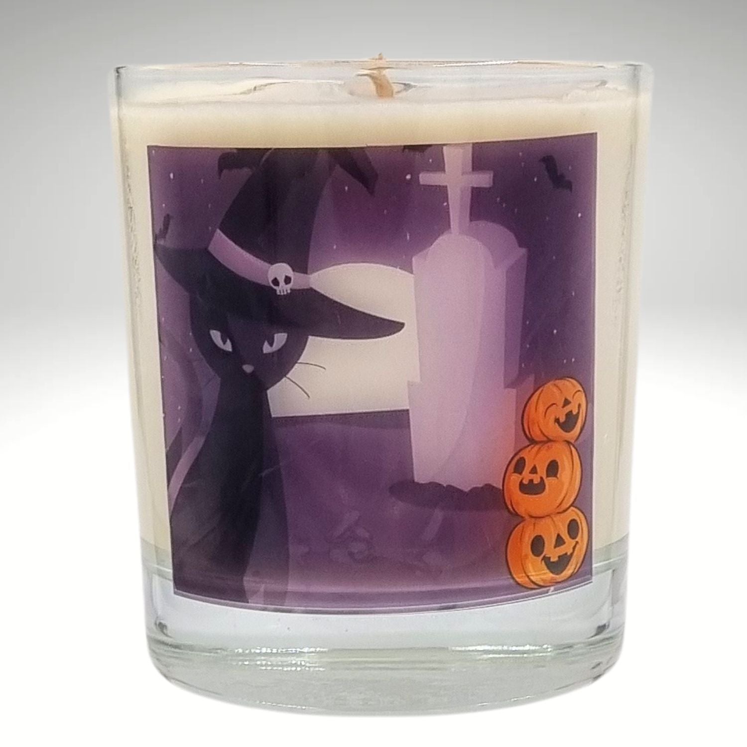 glass container halloween candle with black cat in witches hat in a graveyard with pumpkins