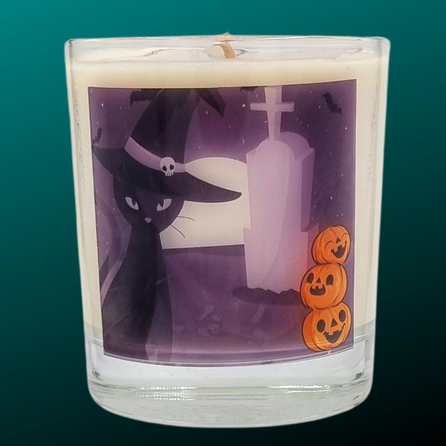 glass container halloween candle with black cat in witches hat in a graveyard with pumpkins