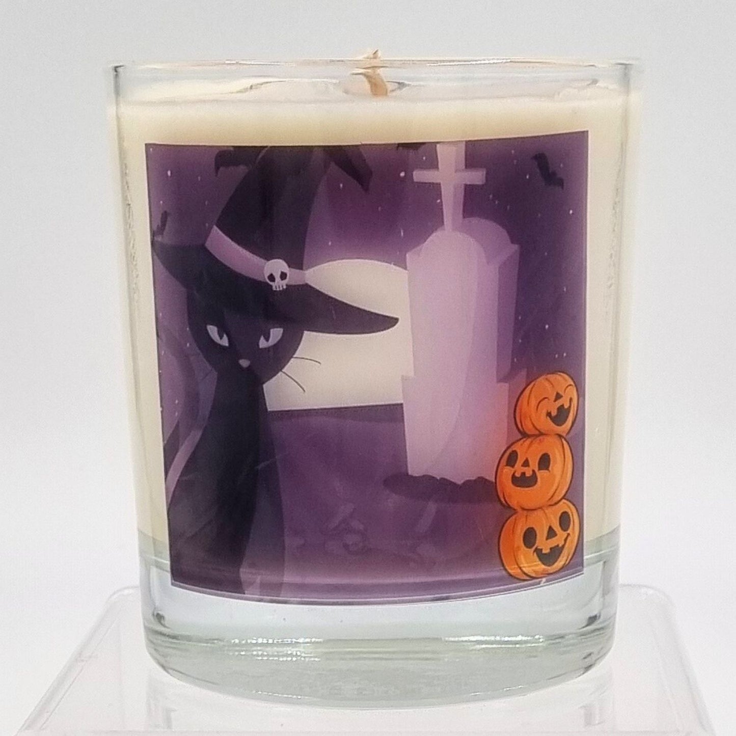 glass container halloween candle with black cat in witches hat in a graveyard with pumpkins