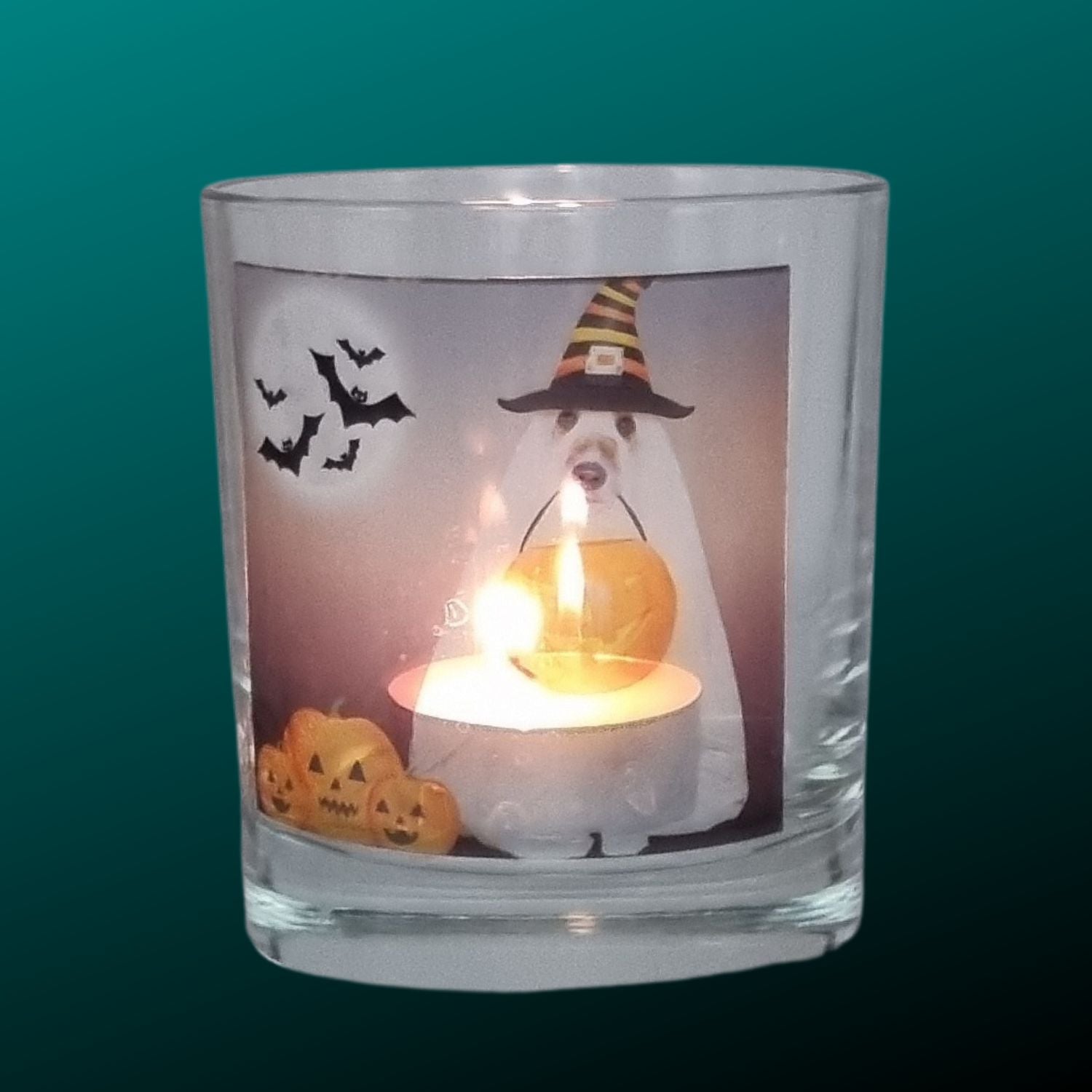 A Halloween tealight holder with a lit tealight featuring a spooky dog in a sheet dressed as a ghost with a trick or treat pumpkin bowl