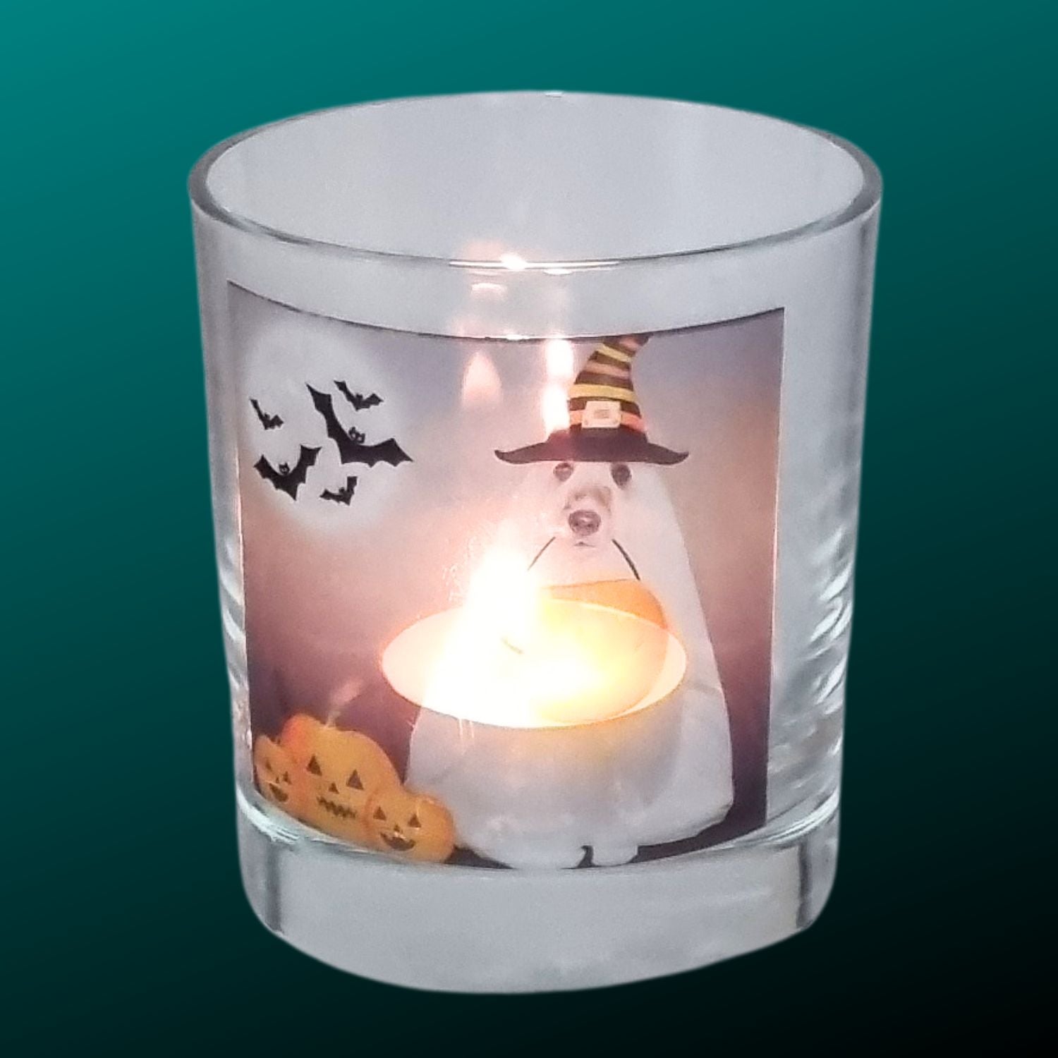 A Halloween tealight holder with a lit tealight featuring a spooky dog in a sheet dressed as a ghost with a trick or treat pumpkin bowl