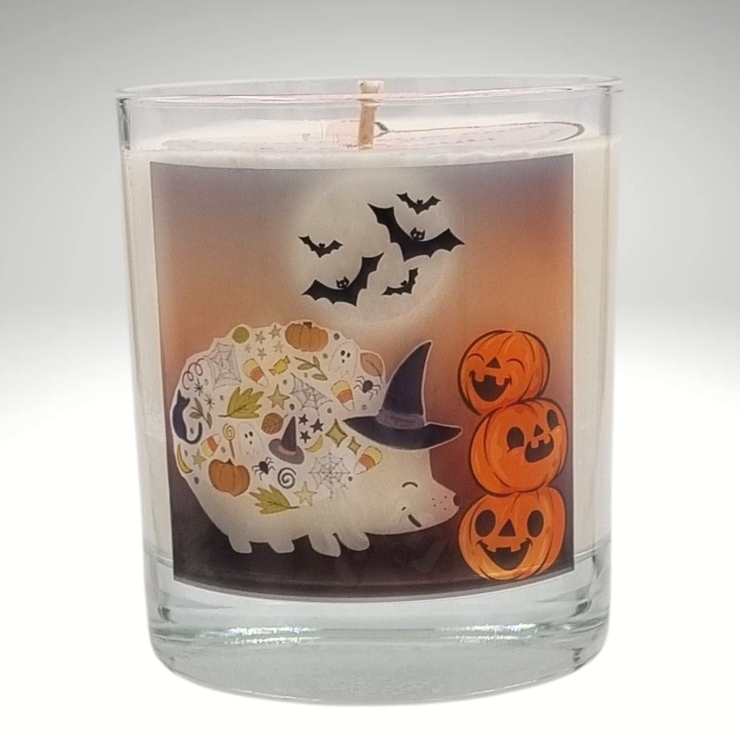 a scented halloween candle in glass with a cute hedgehog in a witches hat with pumkins and bats