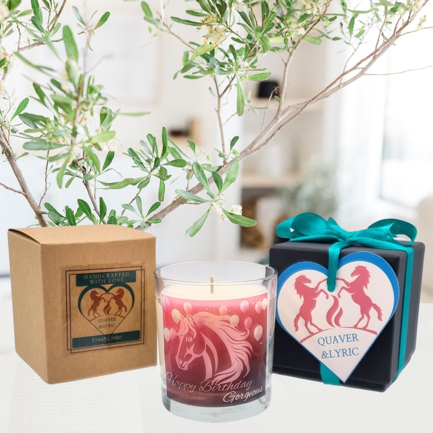 A Quaver&Lyric Happy Birthday Gorgeous horse design scented candle in a glass container, presented in a brown gift box, with a heart ornament featuring two unicorns and Quaver & Lyric, displayed by a leafy plant.