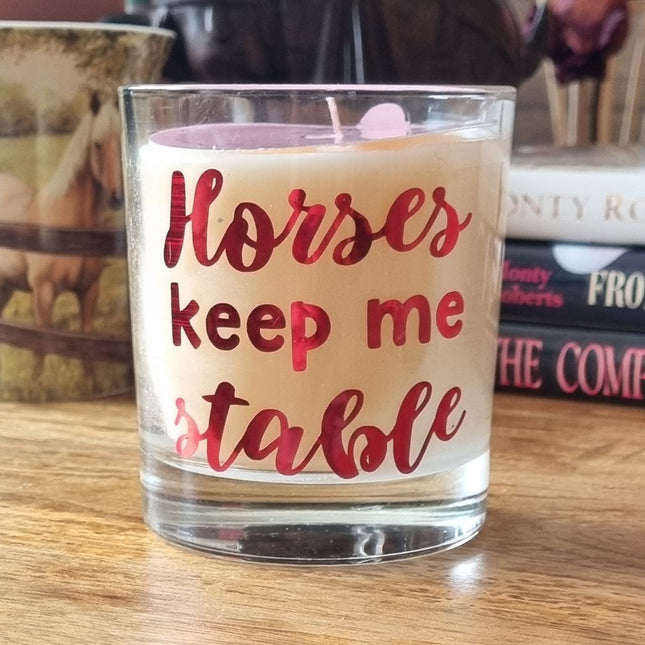 The Quaver&Lyric Scented Candle in a glass holder features the Horses Keep Me Stable designâ€”an ideal gift for horse lovers. Displayed on wood, itâ€™s surrounded by horse-themed dÃ©cor like a mug and books about horses.